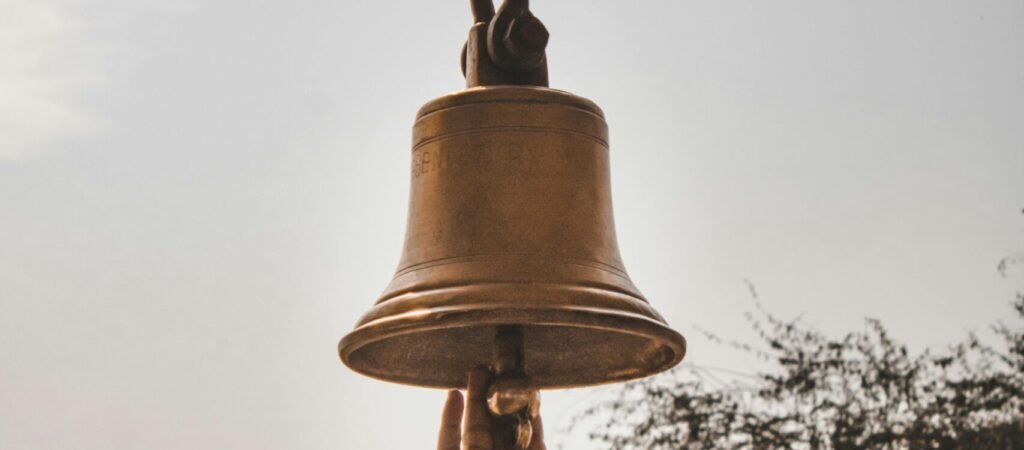 A hand reaches up to ring a bell outdoors in Jaisalmer, Rajasthan, India.